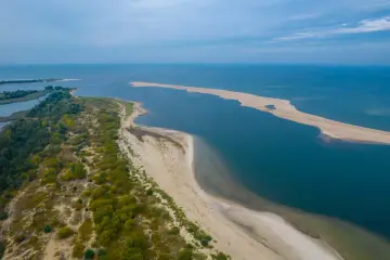 Piękna plaża i turkusowe morze – idealne miejsce, gdzie nad morze. Długi, piaszczysty cypel otoczony wodą, z zielenią po lewej stronie.